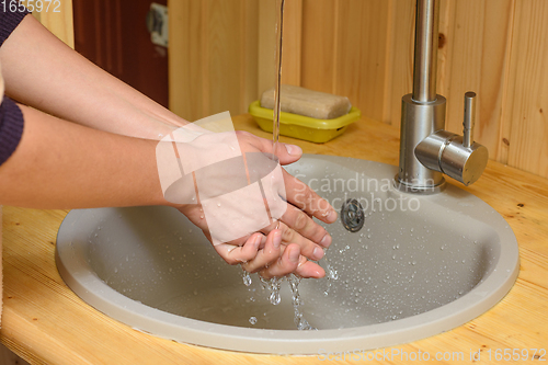 Image of The girl washes her hands under running water in the sink