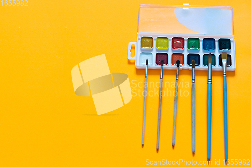 Image of Watercolor paints and brushes of different sizes lie on an orange background