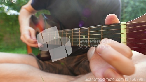 Image of Man sitting in the grass playing guitar