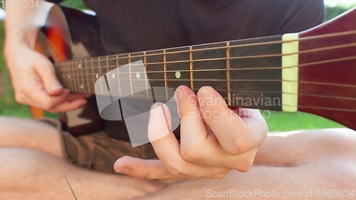 Image of Man sitting in the grass playing guitar