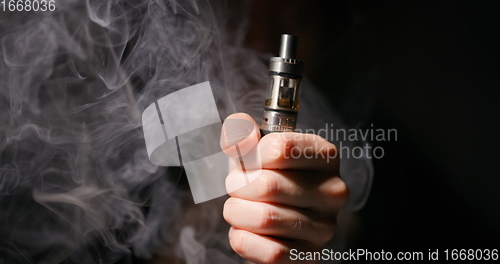 Image of Electronic cigarette grabbed by male hand against dark background and vapor