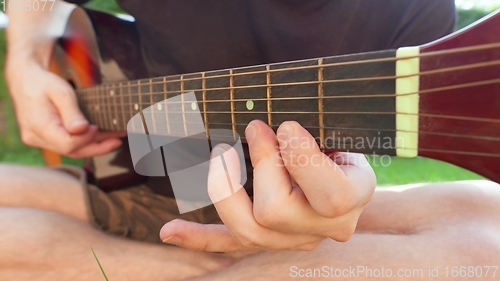 Image of Man sitting in the grass playing guitar