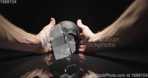 Image of Hands reaching for black skull with reflection