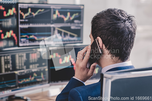 Image of Over the shoulder view of stock broker trading online, talking on mobile phone.