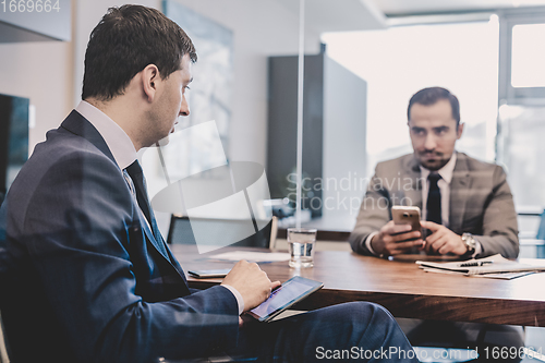 Image of Two businessmen using smart phones and touchpad at meeting.