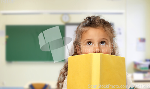 Image of little girl hiding behind yellow book at school