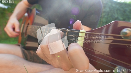 Image of Man sitting in the grass playing guitar