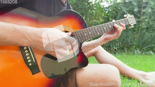 Image of Man sitting in the grass playing guitar