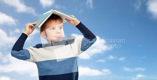 Image of little boy with roof of book on his head over sky