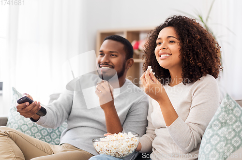 Image of african couple with popcorn watching tv at home