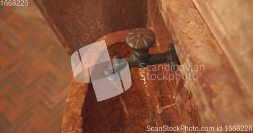 Image of Old stone wash basin with decorative tap with water flowing