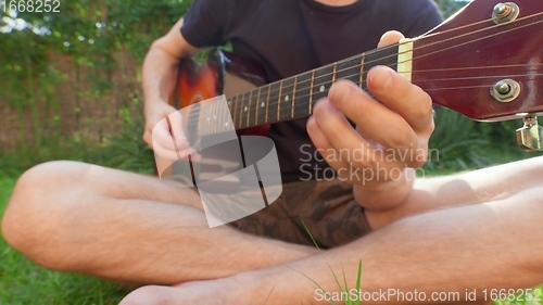 Image of Man sitting in the grass playing guitar