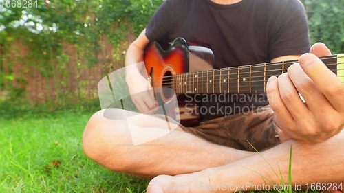 Image of Man sitting in the grass playing guitar