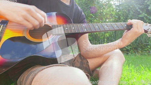 Image of Man sitting in the grass playing guitar