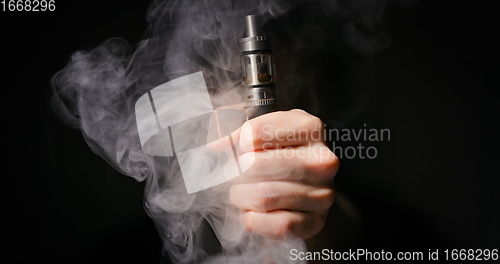 Image of Electronic cigarette grabbed by male hand against dark background and vapor