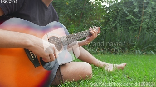 Image of Man sitting in the grass playing guitar