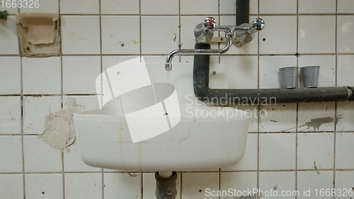 Image of Old wash basin on tiled wall leaking water