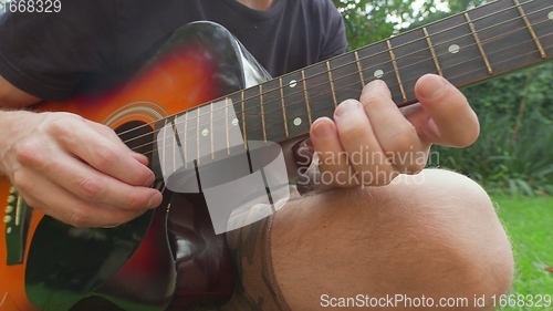 Image of Man sitting in the grass playing guitar