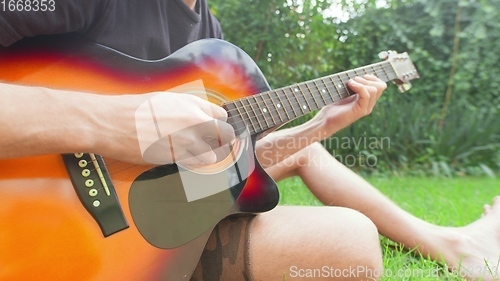 Image of Man sitting in the grass playing guitar