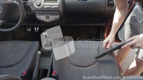 Image of Man cleaning dirty car interior with vacuum cleaner