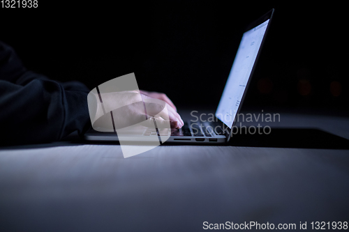 Image of hacker using laptop computer while working in dark office