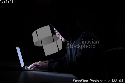 Image of hacker using laptop computer while working in dark office