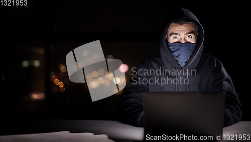 Image of hacker using laptop computer while working in dark office