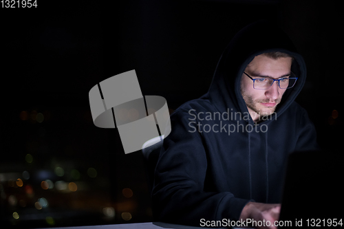 Image of hacker using laptop computer while working in dark office