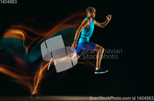 Image of Professional male runner training isolated on black studio background in mixed light