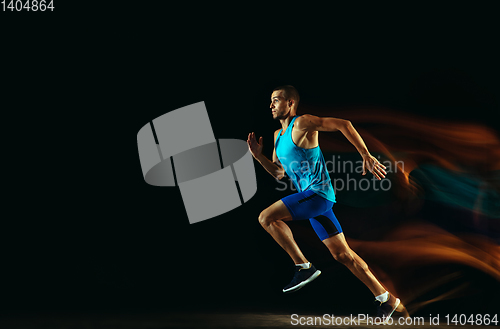 Image of Professional male runner training isolated on black studio background in mixed light