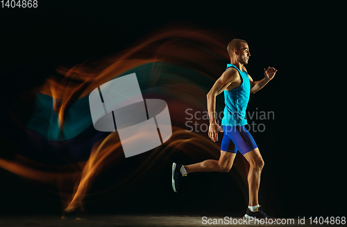 Image of Professional male runner training isolated on black studio background in mixed light