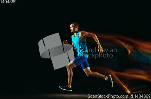 Image of Professional male runner training isolated on black studio background in mixed light