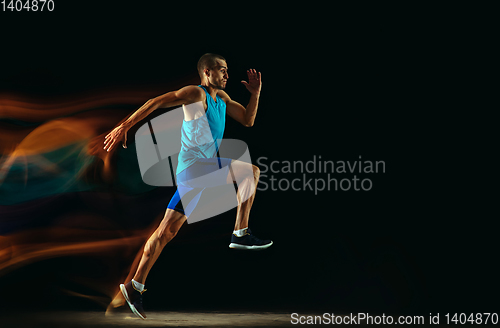 Image of Professional male runner training isolated on black studio background in mixed light