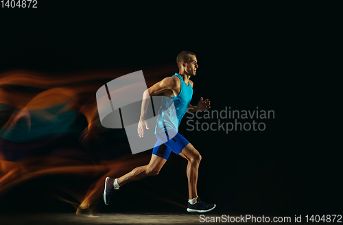 Image of Professional male runner training isolated on black studio background in mixed light