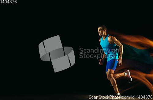 Image of Professional male runner training isolated on black studio background in mixed light