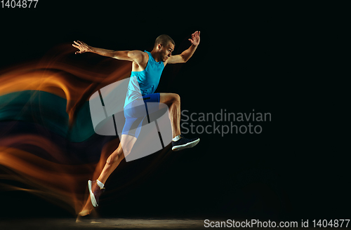 Image of Professional male runner training isolated on black studio background in mixed light