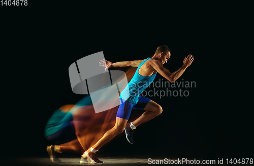 Image of Professional male runner training isolated on black studio background in mixed light