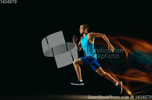 Image of Professional male runner training isolated on black studio background in mixed light