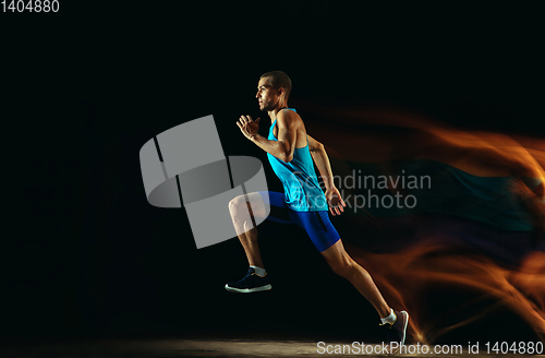 Image of Professional male runner training isolated on black studio background in mixed light