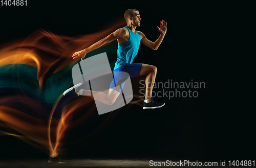 Image of Professional male runner training isolated on black studio background in mixed light