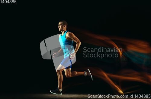 Image of Professional male runner training isolated on black studio background in mixed light