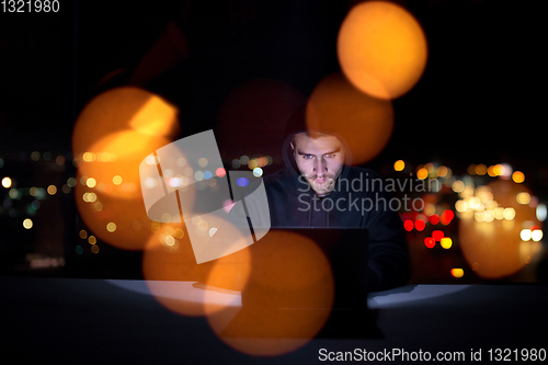 Image of hacker using laptop computer while working in dark office