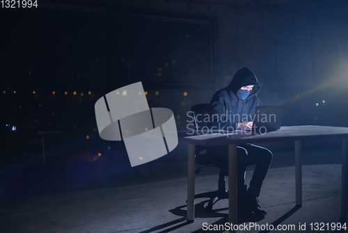 Image of hacker using laptop computer while working in dark office