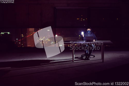 Image of hacker using laptop computer while working in dark office