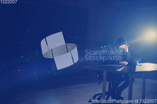 Image of hacker using laptop computer while working in dark office