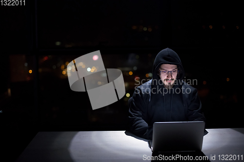 Image of hacker using laptop computer while working in dark office