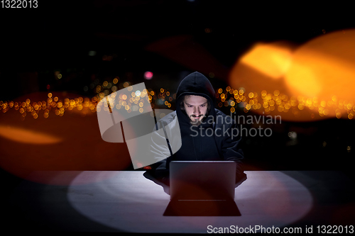 Image of hacker using laptop computer while working in dark office