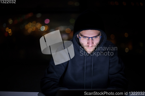 Image of hacker using laptop computer while working in dark office