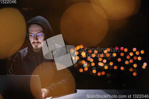 Image of hacker using laptop computer while working in dark office