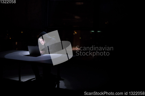 Image of hacker using laptop computer while working in dark office